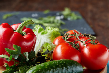 Close-up still life of assorted fresh vegetables and herbs on dark wooden background, top view, shallow depth of field.