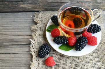 Raspberries and blackberries tea with fresh picked berries in a glass transparent cup on old wooden table.Natural herbal beverage.