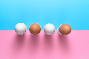 Eggs standing on egg cup on blue and pink pastel background, copy space. Boiled eggs in stand on paper background with two tone color. Healthy food concept. Easter eggs. Flat lay, top view