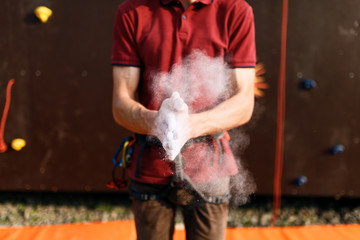 Obraz na płótnie Canvas Close up of climber man coating hands in powder chalk magnesium and preparing to climb outdoor training rock wall. Powder in the air after clapping hands
