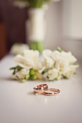 Two gold wedding rings with on a white background with a wedding bouquet