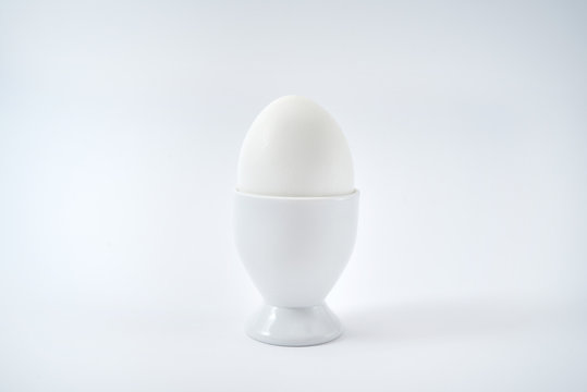 White egg standing on egg cup isolated on white background, copy space. Boiled egg in stand. Healthy food concept, minimalism