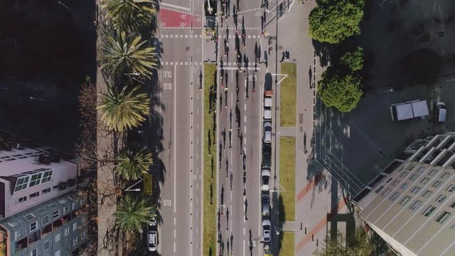 Aerial cinematograph looped shot of many competitors running on city half marathon event on closed urban streets. Surrealistic above wiew with long shadow silhouettes. Motivational video