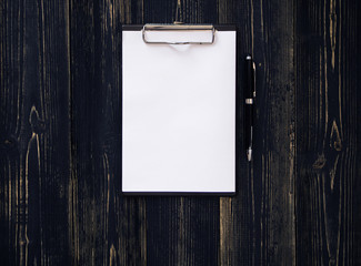Clipboard with white sheet on wood background. Top view.Vintage style.