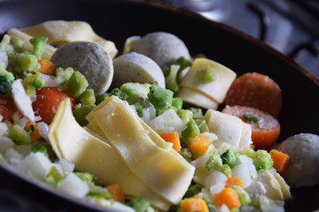 frozen tagliatelle pasta with vegetables in a pan, cream-herb sauce, tomatoes