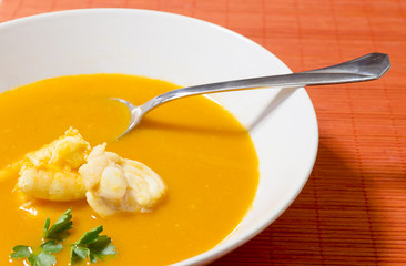 Beautiful presentation of the fish soup in a white plate on a orange background. View from above.