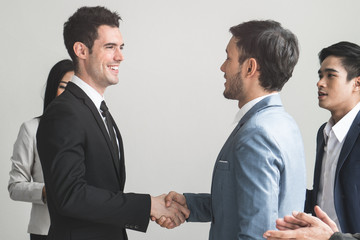 Business partner agreement success concept.Two businessmen shaking hands after seal a deal in the meeting and their staff team congratulation on background, Business partnership concept.