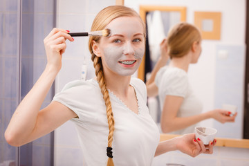 Woman applying with brush clay mud mask to her face