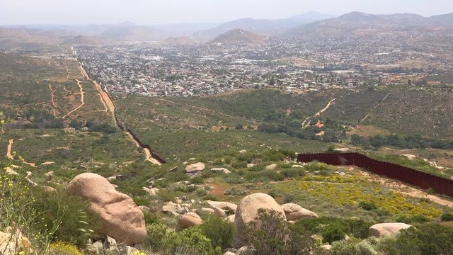 The U.S. border wall fence with the city of Tecate Mexico background.