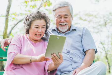 Fototapeta na wymiar elderly people lifestyles and communication technology. Happy grandparent using tablet video call and talking with family in the park.