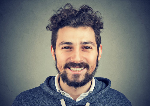 Young hipster man in gray hoodie smiling happily at camera. 