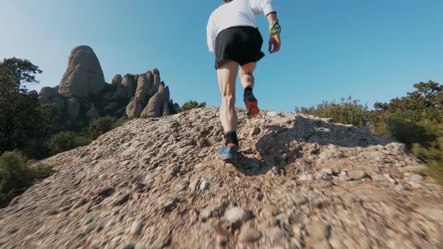 Low angle slow motion action sports shot of strong and muscular man in sports outfit run up steep rock or cliff during ultra marathon trail running workout training or competition in epic landscape.