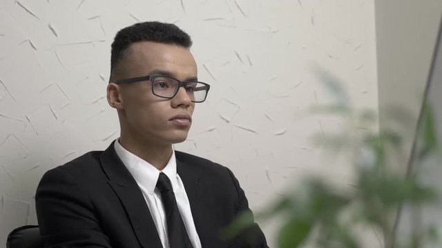 Young successful businessman in glasses works on the computer in the office, smiles and looks at the camera 60 fps