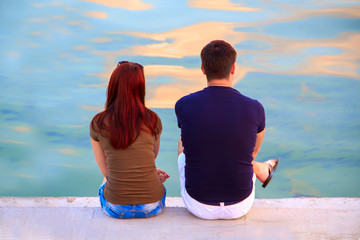 Fototapeta premium A guy in a T-shirt and shorts and a girl in a T-shirt and jeans are sitting on a concrete slab on the river bank.