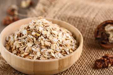 Dry rolled oatmeal in wooden bowl on textile background.