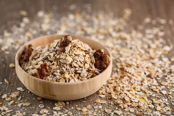 Dry rolled oatmeal in wooden bowl on oatmeal background.