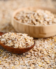 Dry rolled oatmeal in wooden bowl and wooden spoon on oatmeal background. Top view.