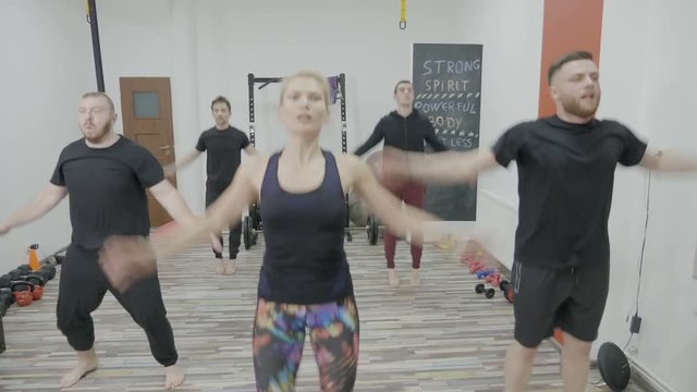 Young men on zumba class warming up by dancing in a gym studio led by a female instructor