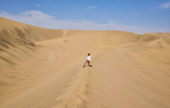 Boy with sandboard looking out over sand dunes, Ica, Peru