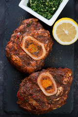 Above view of raw marinated cross cut veal shanks with gremolata on a stone slate, closeup, vertical shot