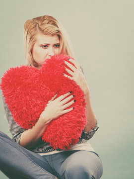 Sad woman holding red pillow in heart shape