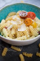 Close-up of boiled fusilli with parmesan and cherry tomatoes, selective focus, studio shot