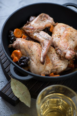 Cast-iron pan with rabbit stewed in white wine with addition of prunes, carrot and onion, selective focus