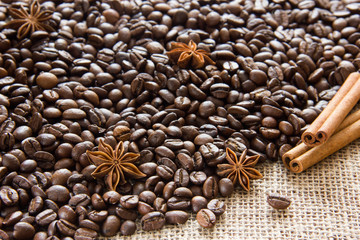 Roasted coffee beans are scattered on sackcloth with anise and cinnamon sticks