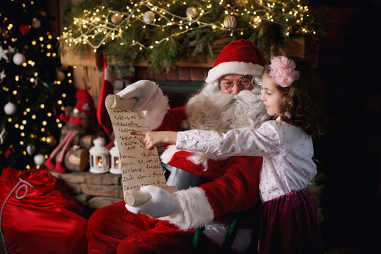 Young girl visiting Santa, pointing to list
