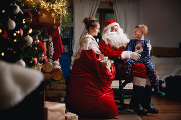 Young girl and boy sitting with Santa, sack full of presents beside him
