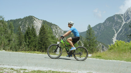 Fototapeta premium Cheerful cyclist riding his electric bicycle up a hill in the sunny mountains.