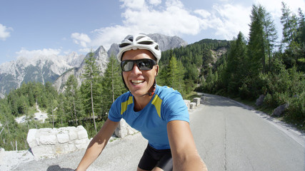 SELFIE: Caucasian man smiles into the camera as he rides up a steep mountain.