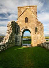 Ruins of Oratory of Saint Molaise abbey on Devenish Island with green lawn in foreground....