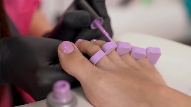Applying the polish to toenails. Closeup of woman feets. Beaty salon. Pedicure.