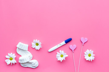 Pregnancy test, socks and flowers pink background top view mock up
