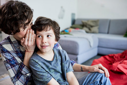 Mother and son at home, mother whispering into son's ear