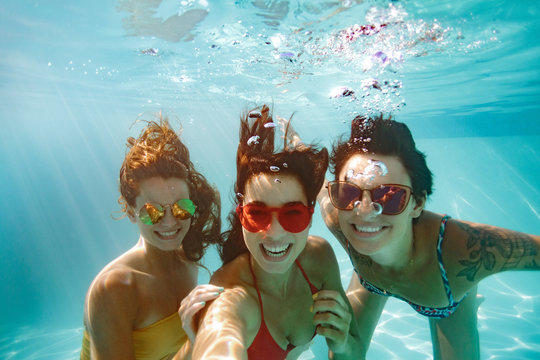 Cheerful friends making selfie underwater in pool