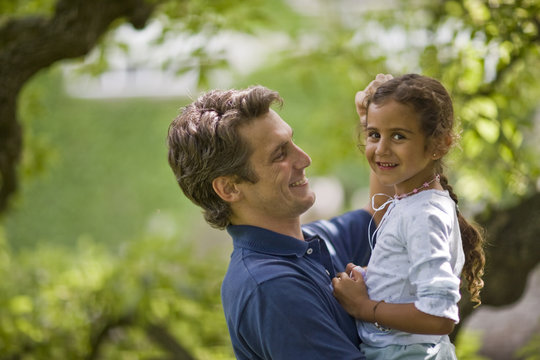 Portrait of a smiling young girl being held by her father while outside in the garden.