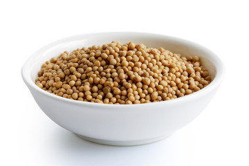 Dried white mustard seeds in white ceramic bowl isolated on white.