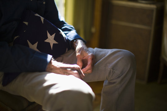Mid section of a senior man with folded American flag sitting at home