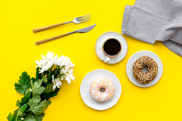 modern breakfast desing with sweet donut, coffee and flowers on woman yellow desk background top view