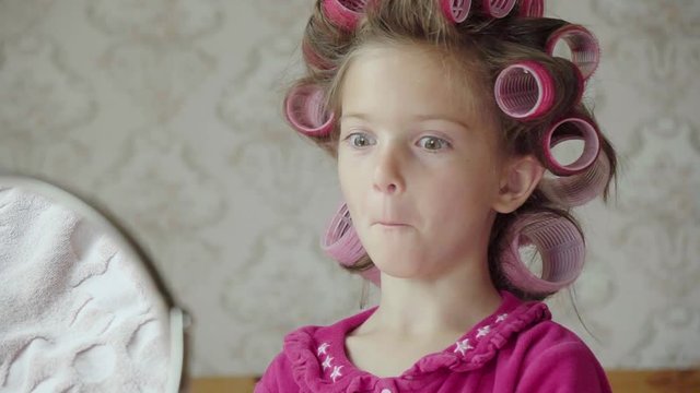 Hilarious girl with hair rollers mimics and laughs at a mirror.