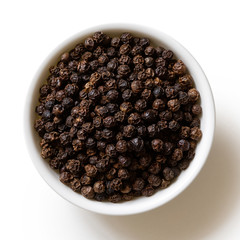 Whole black peppercorns in white ceramic bowl isolated on white from above.