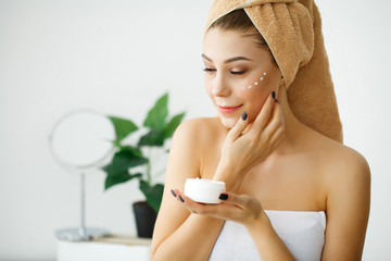 Obraz na płótnie Canvas Skin care. Woman with healthy face applying cosmetic cream under the eyes