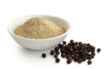 Finely ground white pepper in white ceramic bowl next to black peppercorns isolated on white.