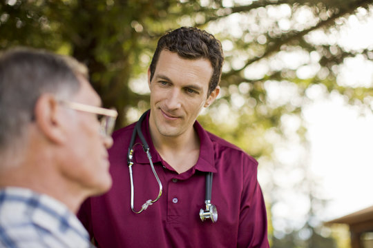 Smiling male nurse assisting an elderly patient outdoors.