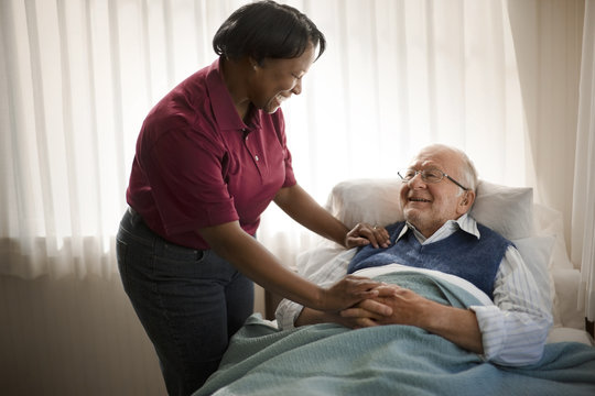 Happy female nurse comforting an elderly patient at his bedside