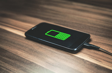 Mobile phone charging on wooden desk.