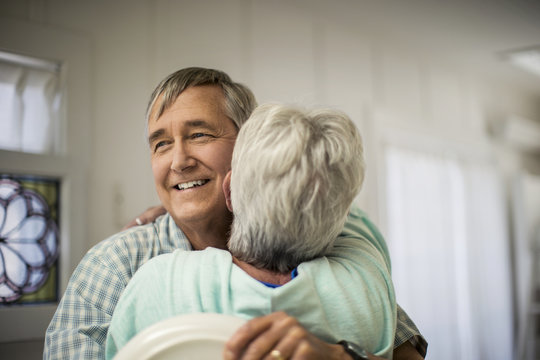 Affectionate mature couple share a spontaneous hug as they finish putting the dishes away.
