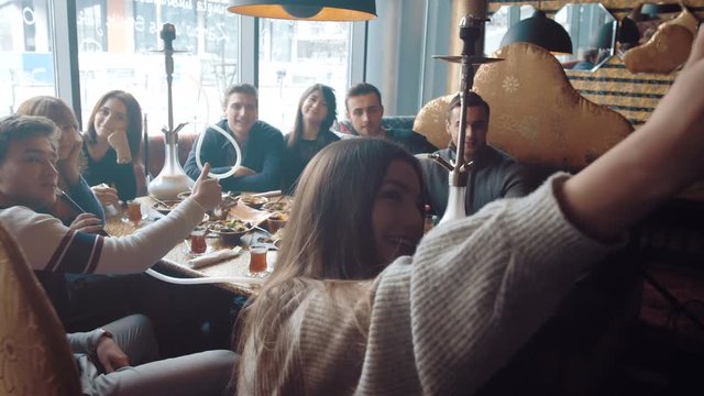 Young company is making selfie. Smoking a hookah and communicating in an oriental restaurant.